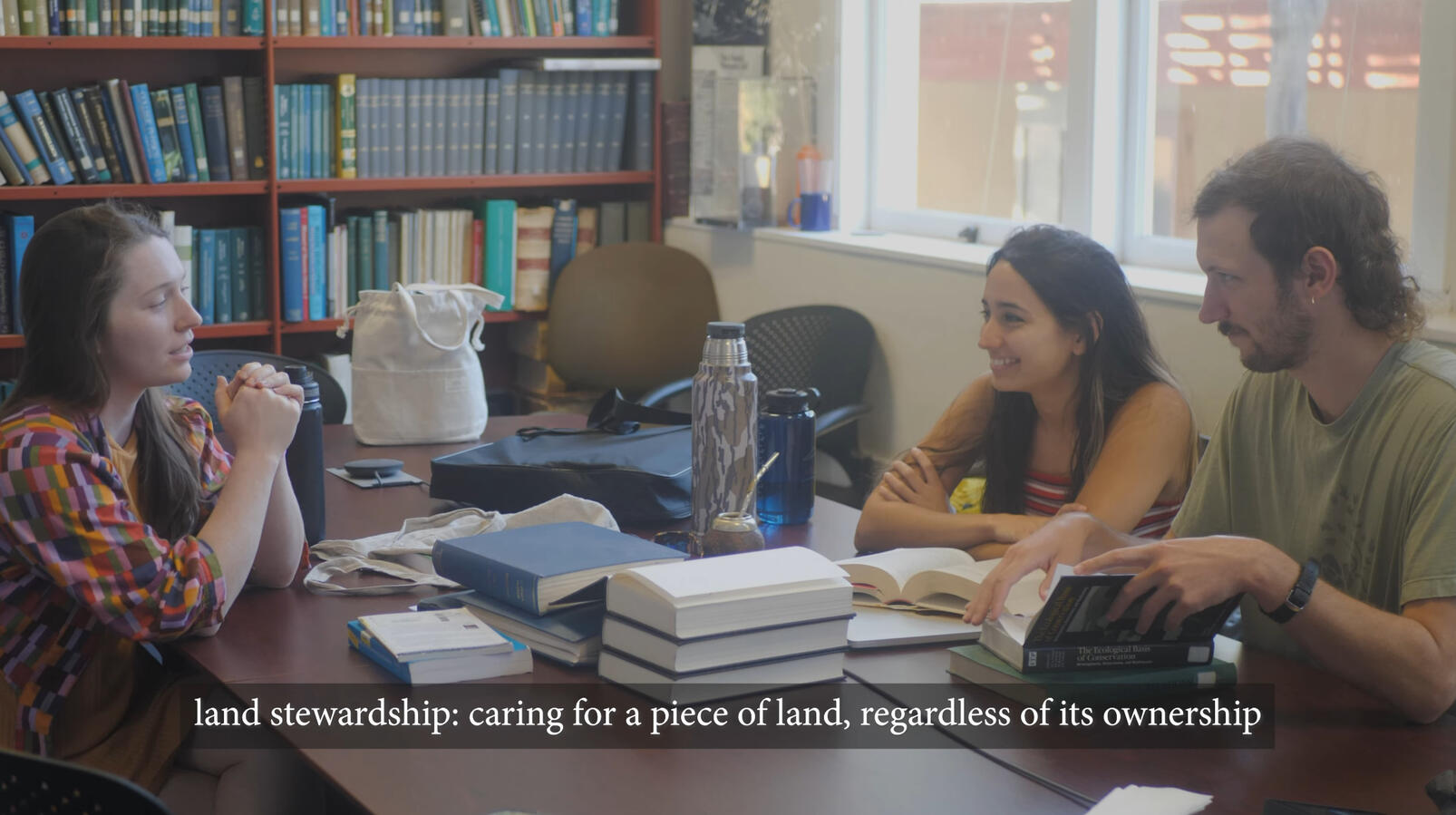 The team meeting in a library room to discuss what to do next, with a definition of land stewardship on screen